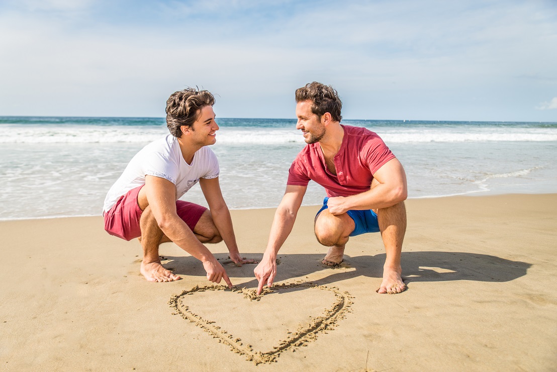 Gay couple drawing a heart on the sand - Homosexual couple walking on the beach on a romantic date